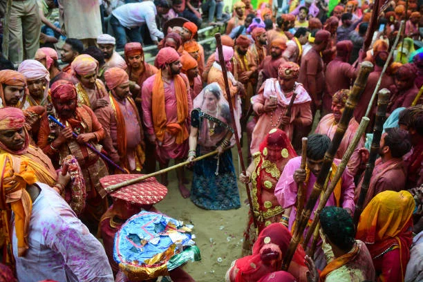 A traditional Lathmar Holi in Mathura, where women dressed in vibrant sarees playfully hit men with sticks as part of the festive celebrations, surrounded by devotees drenched in colors.